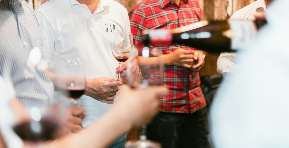 a group of men standing next to each other holding wine glasses