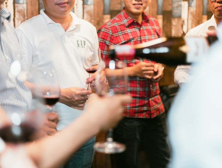 a group of men standing next to each other holding wine glasses
