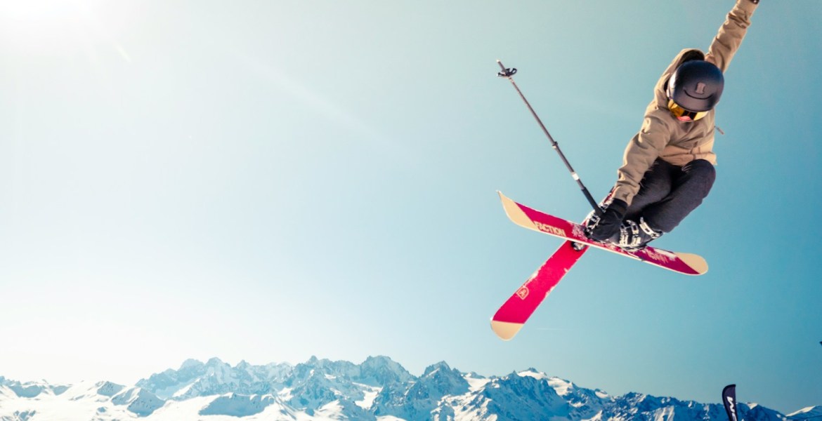 person in brown jacket doing snow ski blade trick