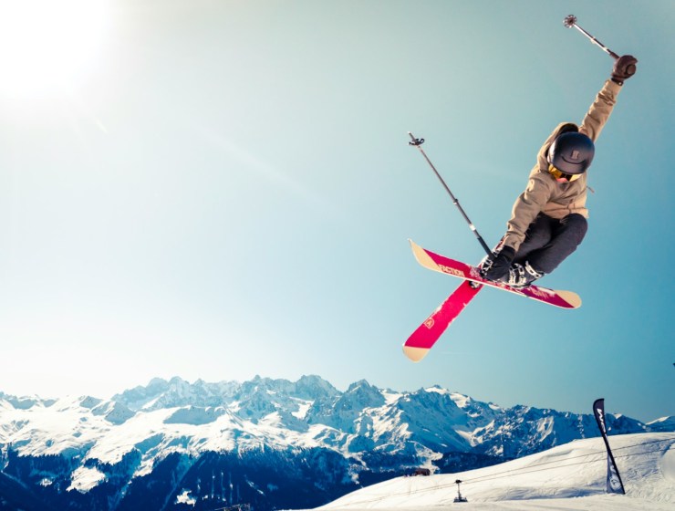 person in brown jacket doing snow ski blade trick