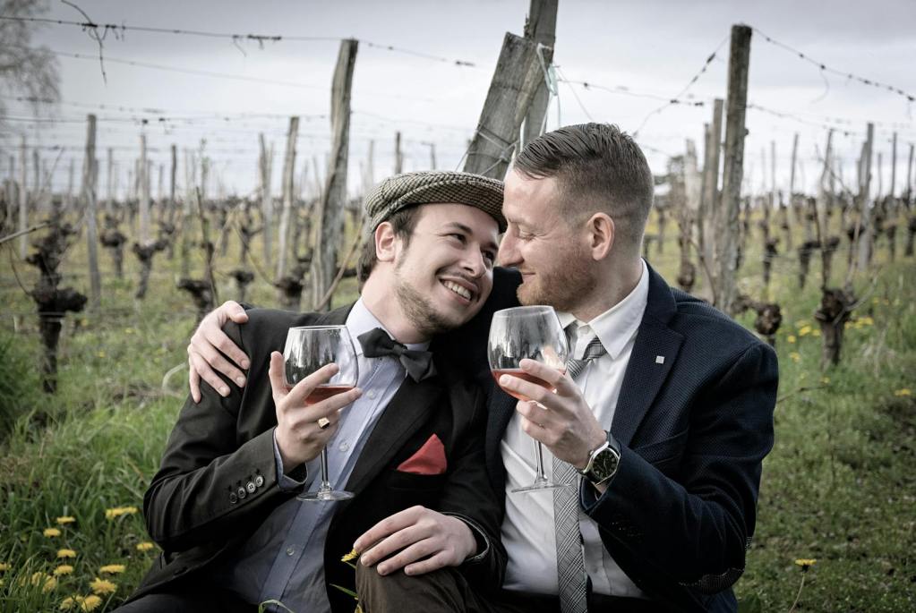 Happy couple in vineyard hugging and sharing a glass of wine, showcasing romance and joy outdoors.