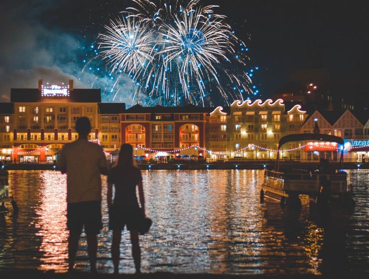 two people standing beside body of water watching fireworks