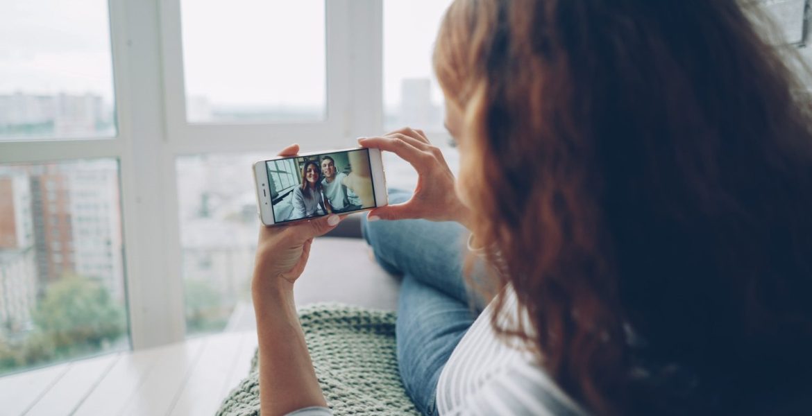 Woman holding phone watching video call by window