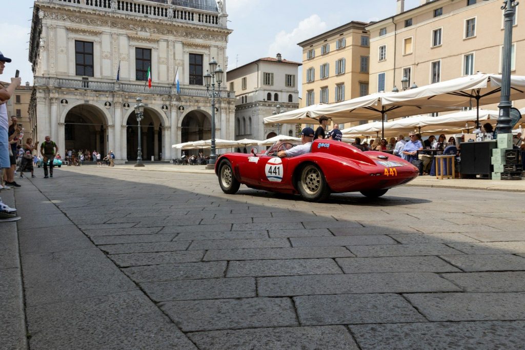 Red vintage race car on cobblestone street in historic city.