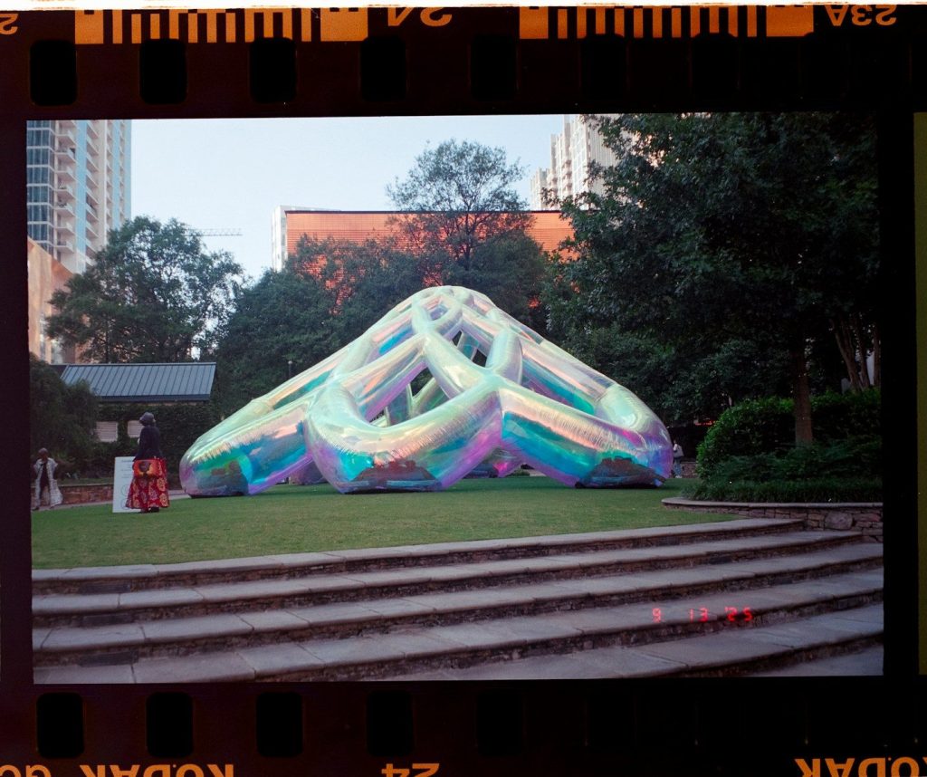Iridescent, futuristic sculpture in a park setting